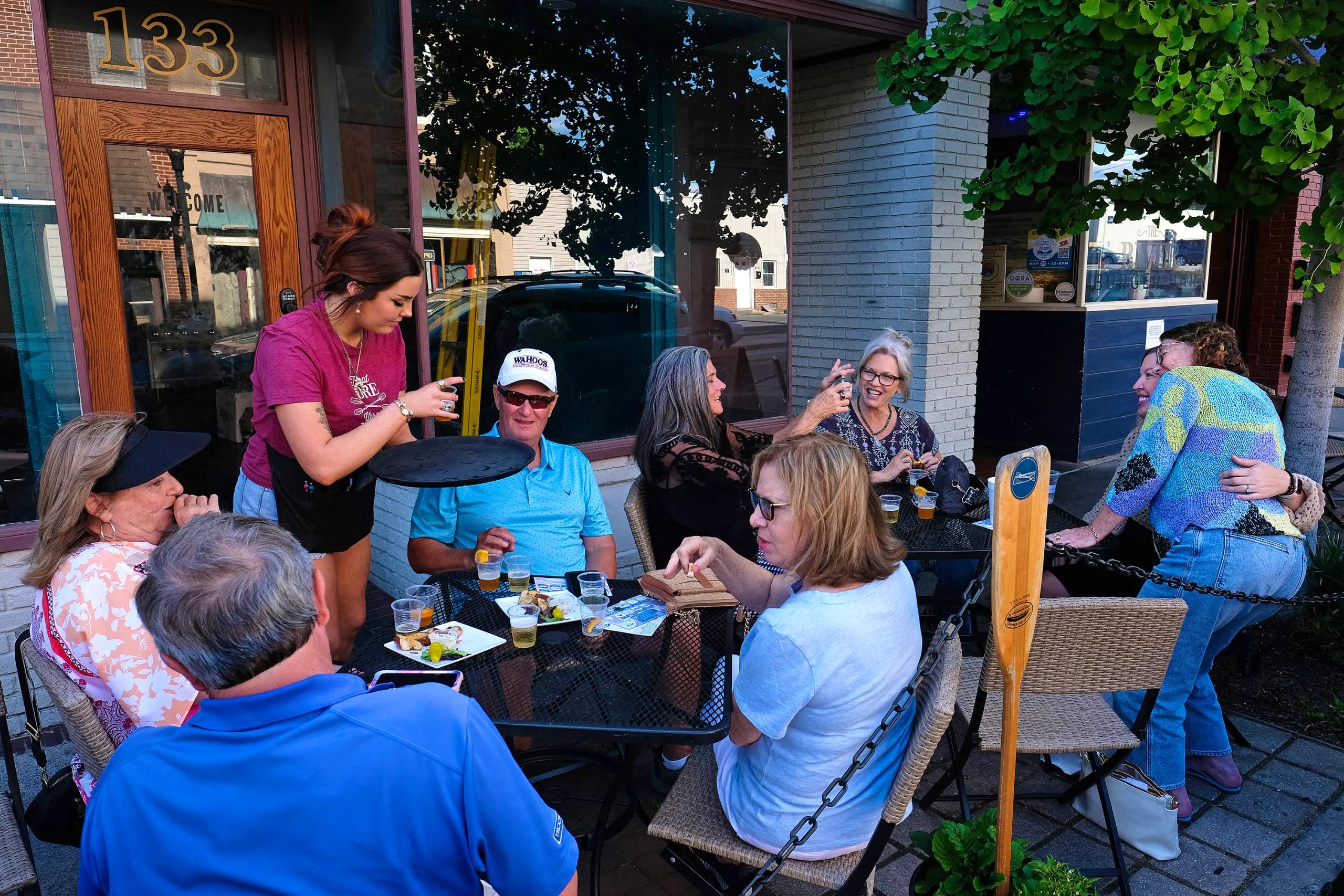 A group of diners at The River Burger Bar's outdoor seating on a city street. A server is passing out drinks.