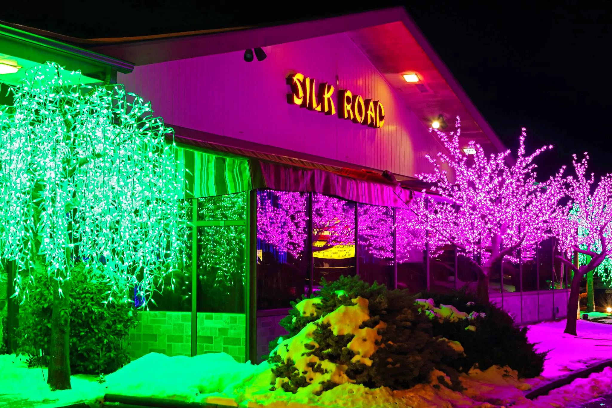 The outside of Silk Road restaurant with neon lights and trees.